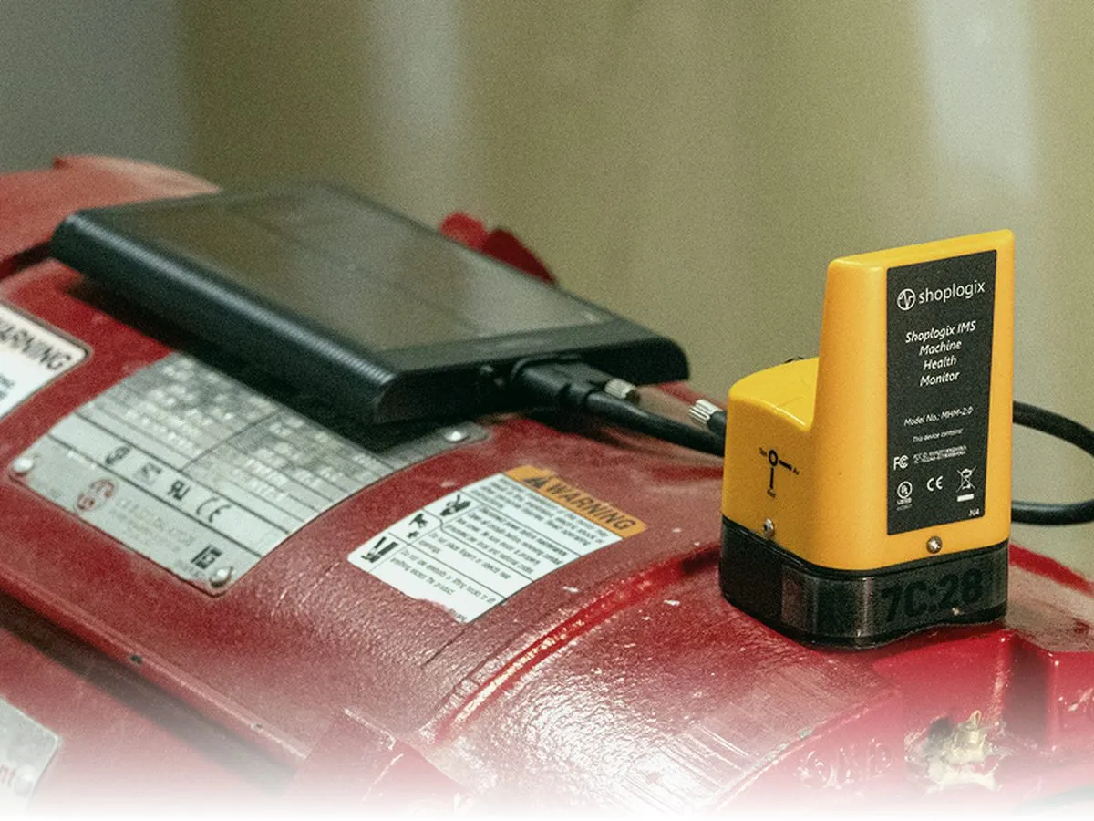 Batteryless wireless vibration sensor (the Everactive MHM platform, ShopLogix-branded variant) mounted on the housing of a red industrial motor next to its warning and rating labels