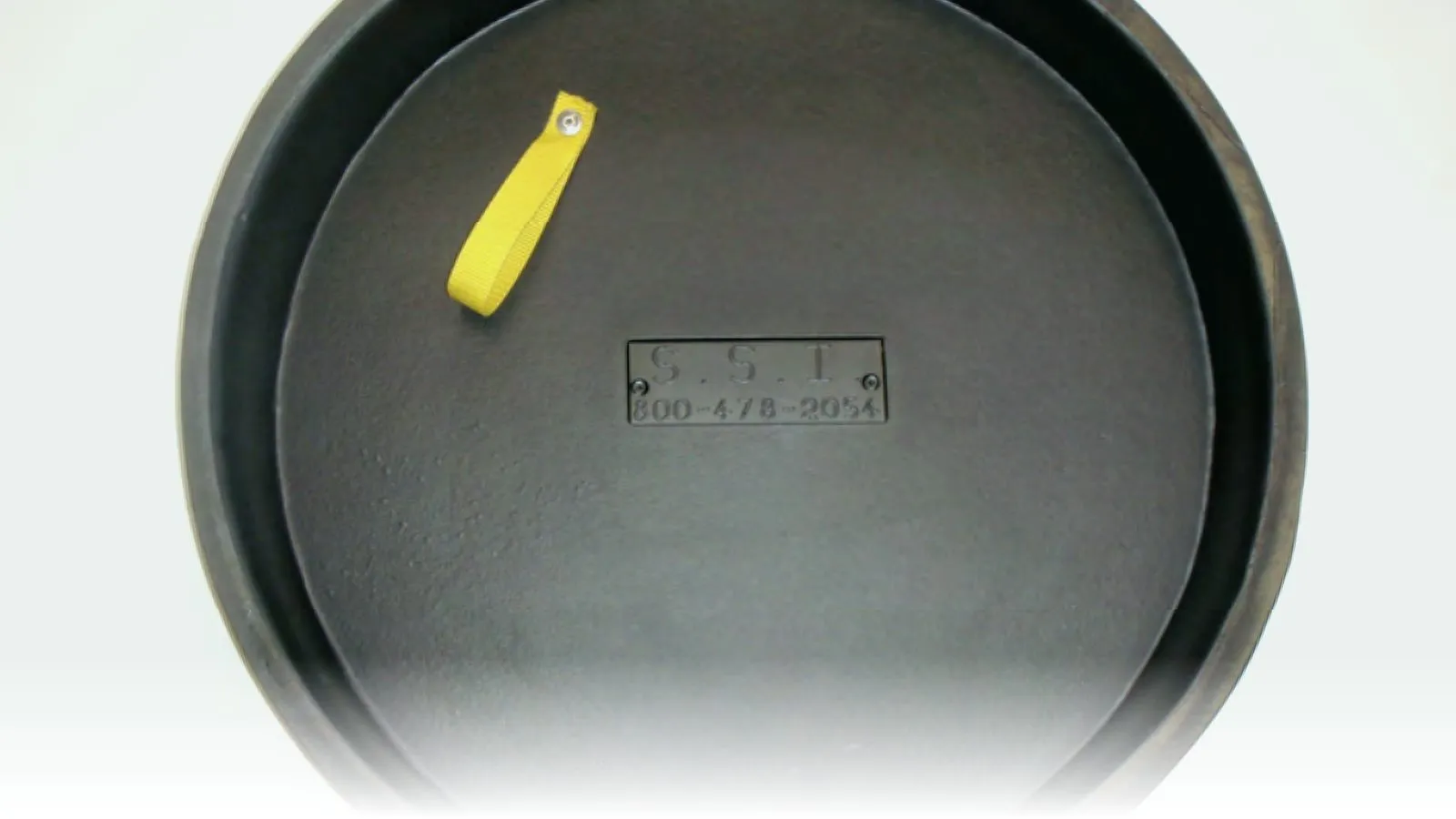 SSI Manhole Insert inflow protector dish photographed from above — black moulded polyethylene dish with raised rim, embossed "S.S.I." nameplate, and a yellow webbing pull-tab for the drain bypass plug